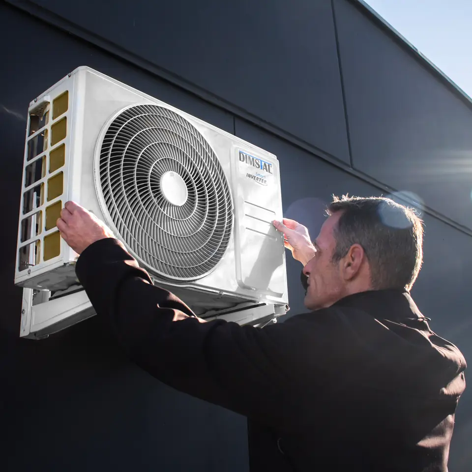 Fachkraft arbeitet an der Außeneinheit einer DIMSTAL Split-Klimaanlage draußen an der Fassade