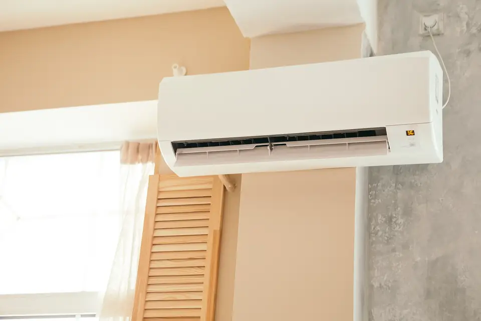 Innengerät einer Split-Klimaanlage an einer hellen Wand neben einem sonnigen Fenster