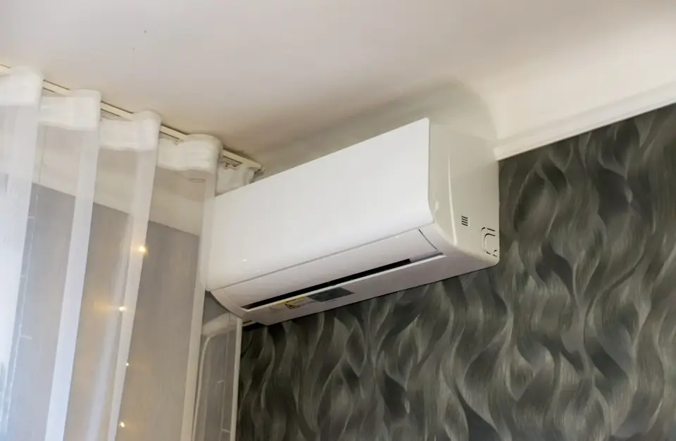 Innengerät einer Split-Klimaanlage an einer gemusterten dunklen Wand neben einem hellen Vorhang