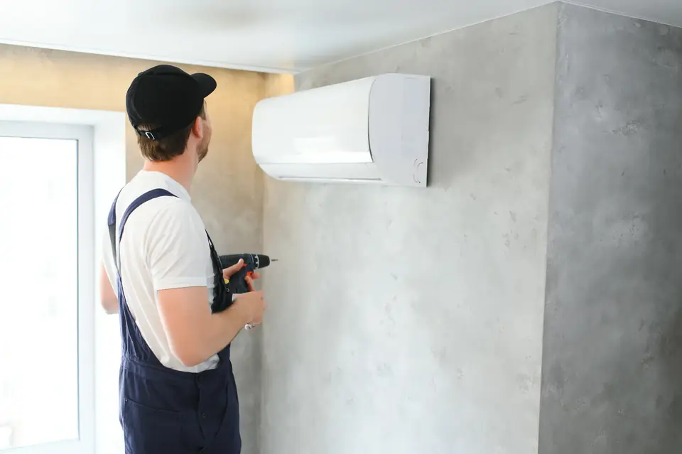 Fachkraft mit Bohrmaschine bereitet die Montage eines Innengeräts an der Wand vor, von hinten fotografiert