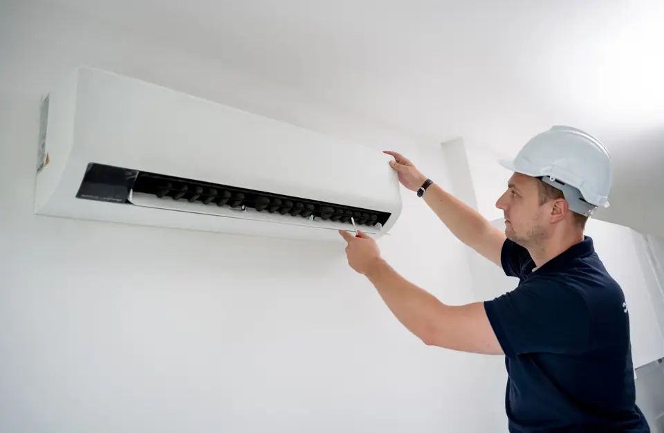 Fachkraft mit Schutzhelm arbeitet am Innengerät einer Split-Klimaanlage in einer Wohnung