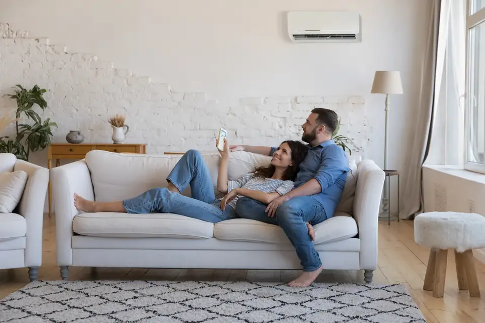Paar entspannt auf dem Sofa in einem hellen Wohnzimmer, an der Wand darüber das Innengerät einer Split-Klimaanlage
